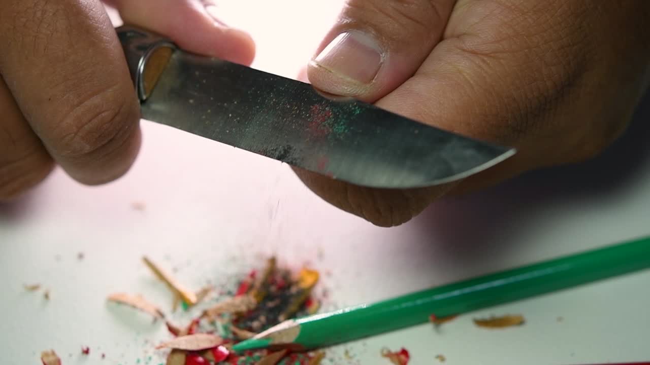 Opptak av hender som sakte spisser en blyant og noen fargeblyanter med en skarp kniv