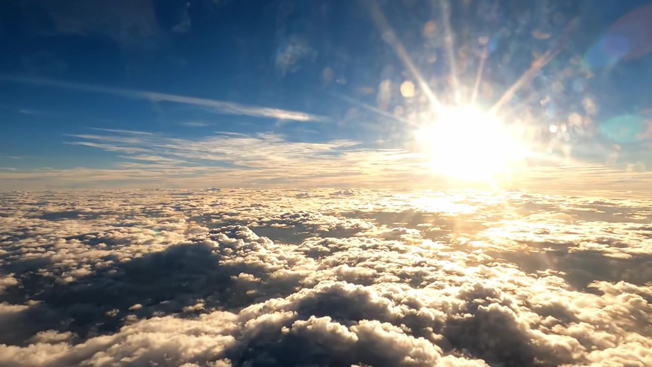 Una splendida vista aerea della luce solare che filtra attraverso un manto di nuvole soffici sotto un cielo blu vibrante, catturata dal finestrino di un aereo.