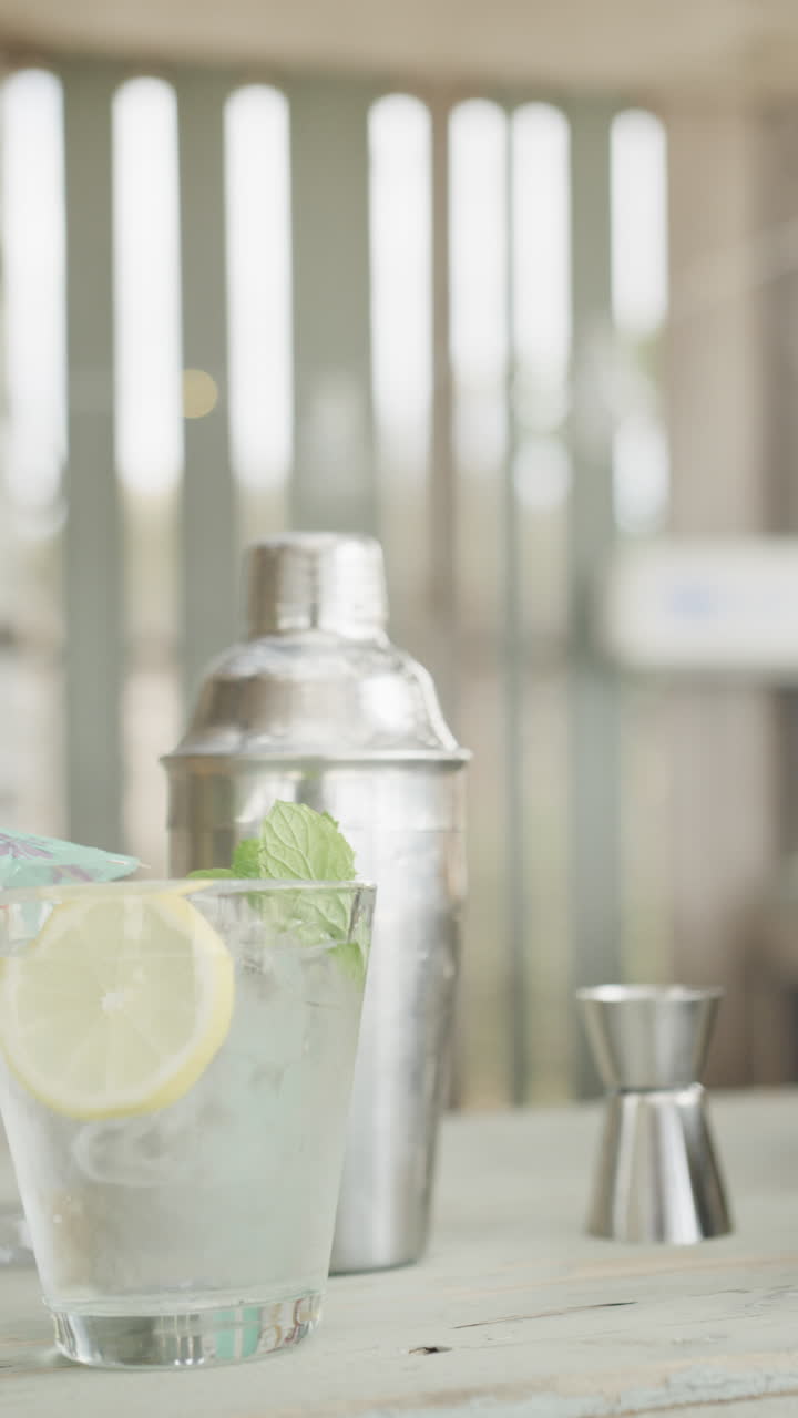 Vertical video of cocktail, cocktail shaker and shot measure on bar at beach bar, slow motion