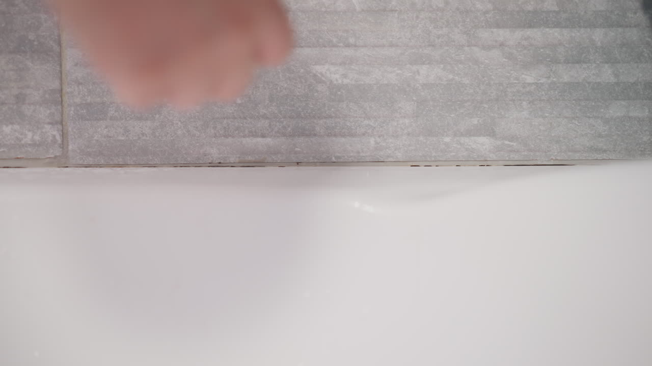 Hand collects fallen hair from walls in bathroom. Person removes remaining hair after taking contrast shower on surface of bathroom