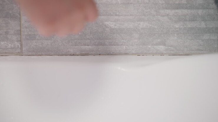 Hand collects fallen hair from walls in bathroom. Person removes remaining hair after taking contrast shower on surface of bathroom