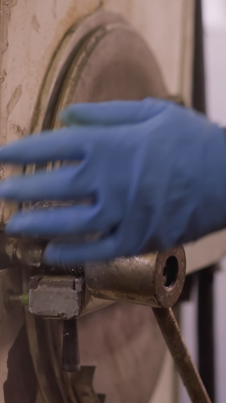 도자기 작업장에서 장갑을 쓴 손으로 오븐 문 레버를 작동하는 노동자, 공예와 수동 노동을 보여줍니다.