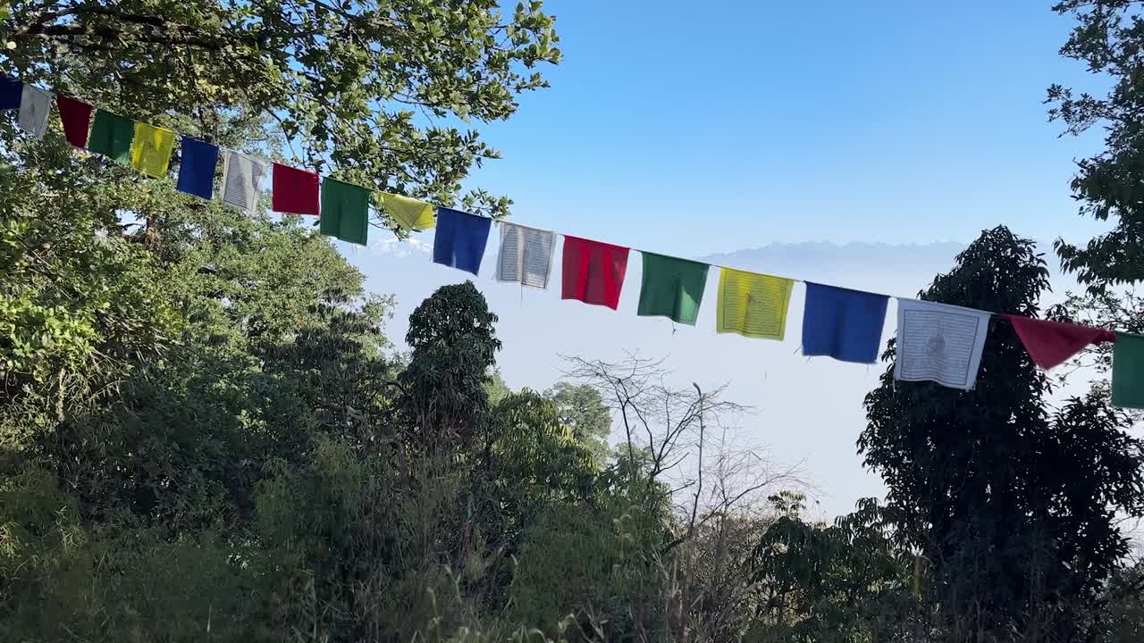 Panning shot of colorful prayer flags with Manaslu, Ganesh, and Langtang mountain ranges seen from Shivapuri Peak, Kathmandu, Nepal.