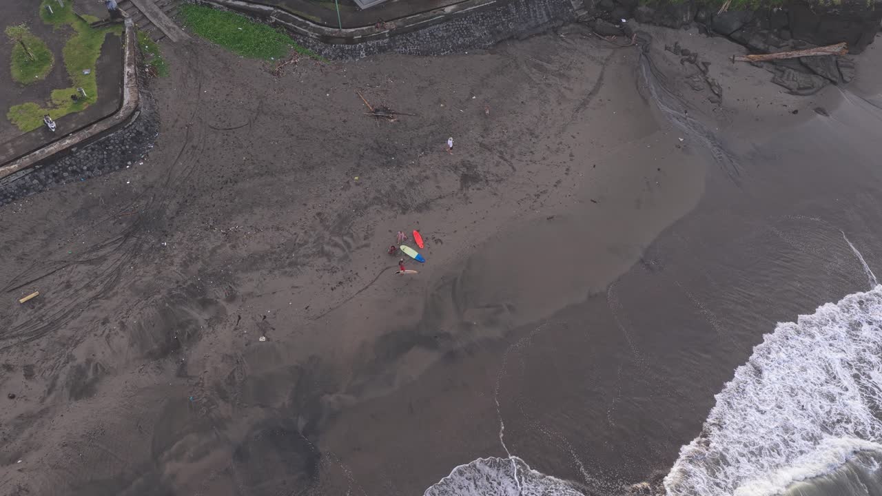 Surfistas caminando en una playa de arena negra en Bali con tablas de surf.