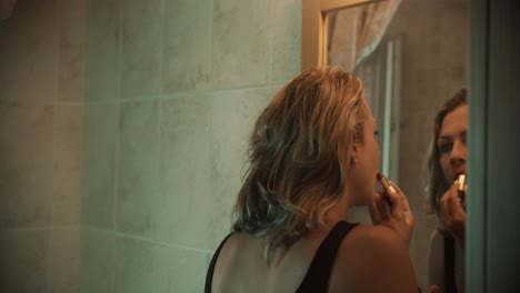 Beautiful-woman-with-black-shirt-applying-red-lipstick-in-front-of-her-bathroom-mirror