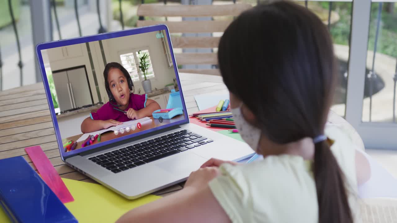 chica de raza mixta sentada en un escritorio usando una computadora portátil teniendo una lección escolar en línea