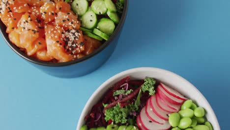 Composition-of-bowls-with-rice,-salmon-and-vegetables-on-blue-background