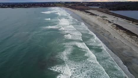 aerial of ocean waves crashing on a beach on a cloudy day