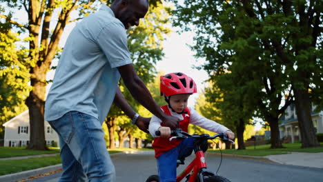 father teaches child to ride a bicycle on a sunny neighborhood street