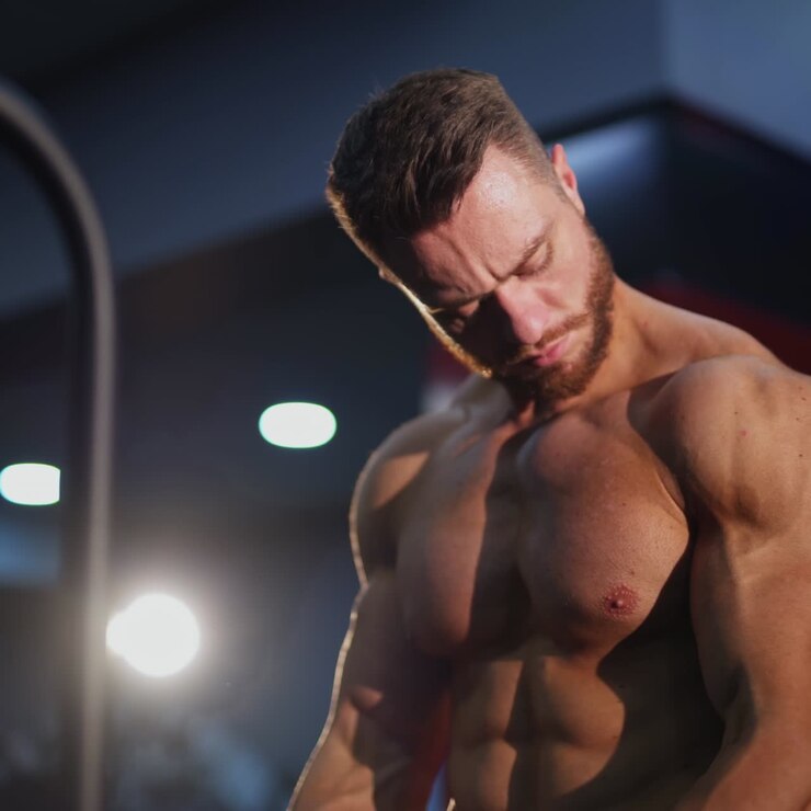 Bodybuilder che allena i muscoli delle braccia. Bel ragazzo con un corpo muscoloso che fa il suo allenamento quotidiano per migliorare i suoi muscoli in palestra. Primo piano.