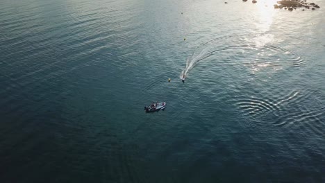 overhead aerial shot of surfer riding electric board past small boat with golden hour light reflection on water surface