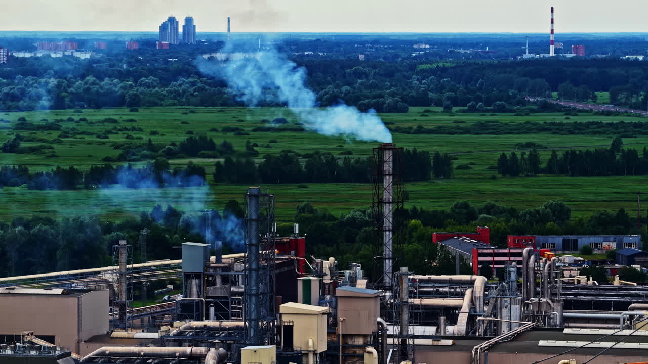 Factory emitting smoke from chimneys in green landscape, aerial view