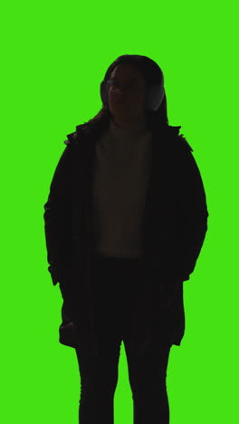 vertical video shot of woman wearing wireless headphones streaming music from mobile phone against green screen with low key lighting 2