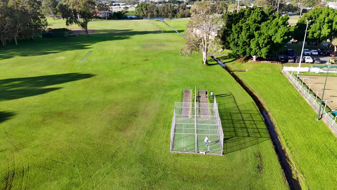 Aerial footage of cricket practice at a lush park in Gold Coast, Australia, captured in bright daylight with clear skies