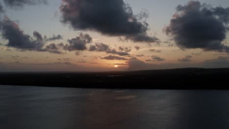 Rising-aerial-shot-of-a-stunning-golden-sunset-from-the-famous-tourist-destination-alligator-beach-at-a-large-river-in-Cabedelo,-Paraiba,-Brazil-near-the-coastal-capital-city-of-Joao-Pessoa