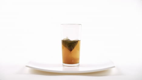 tea infusion in progress with a tea bag steeping in hot water in a clear glass on a plate