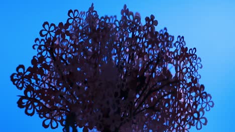 árbol de papel rosa iluminado girando sobre un fondo azul