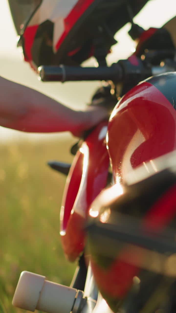 두 사람이 잔디에서 빨간색과 검은색의 오토바이를 청소하는 클로즈업, 오토바이의 우아한 디자인, 특히 연료 크, 그들이 그것을 으면서 초점을 맞추고 있습니다.