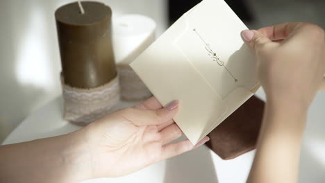 Hermosa-Mano-Femenina-Escribiendo-Una-Invitación-De-Boda-O-Vacaciones-En-Una-Mesa-Blanca-Brillante-Con-Velas