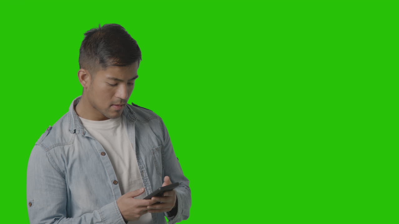 студийный снимок непринужденно одетого молодого человека, обменивающегося сообщениями по мобильному телефону на фоне зеленого экрана 1