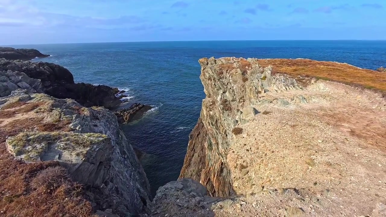 Slow motion fractured coastal rocky cliffs observing blue ocean seascape evokes danger risk idea