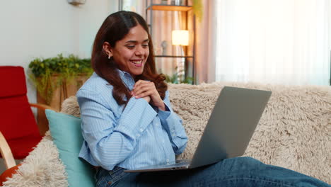 indian woman celebrating good exam result on laptop with joyful jump and hand victory gesture home