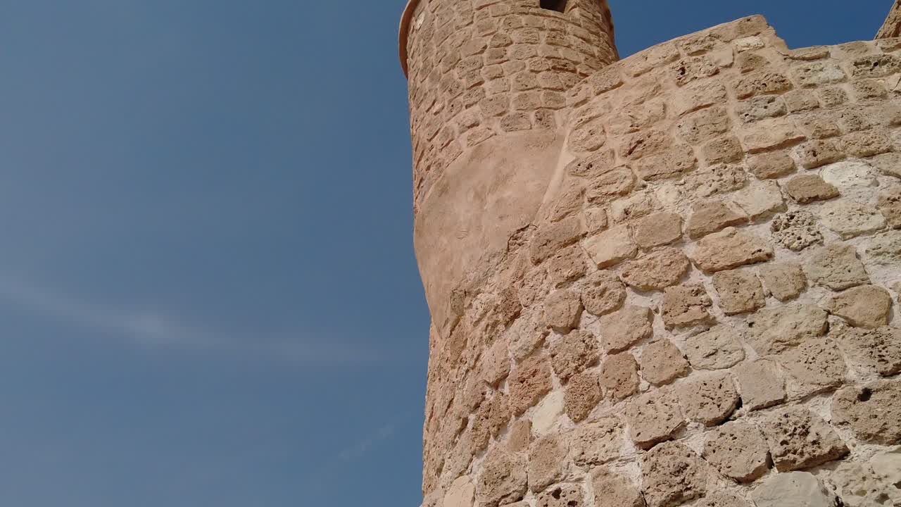 Vista ravvicinata con panoramica verso l'alto di mura storiche in pietra e una torre rotonda di fortezza in Bahrain
