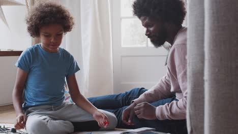 black middle aged father sitting on the floor at home helping his pre-teen son with the instructions for a toy construction kit, close up