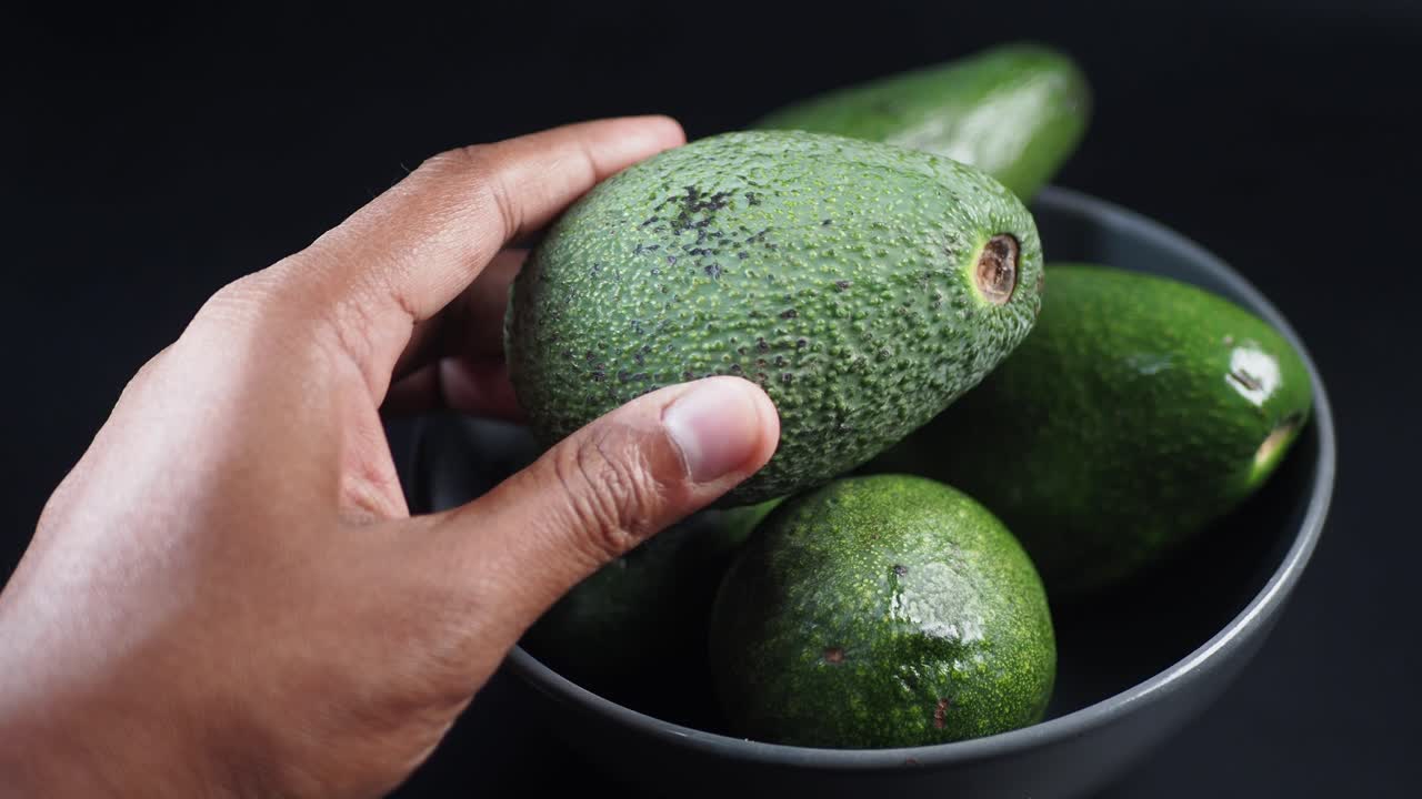 Primo piano di una mano che raccoglie un avocado maturo da una ciotola