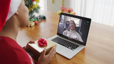 Mujer-Afroamericana-Con-Sombrero-De-Santa-Usando-Una-Computadora-Portátil-Para-Una-Videollamada-Navideña-Con-Una-Mujer-En-La-Pantalla