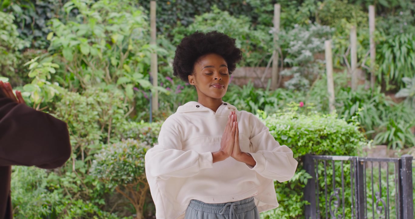 Female friends starting yoga, woman raising lowering palms to chest on porch by railing, centering