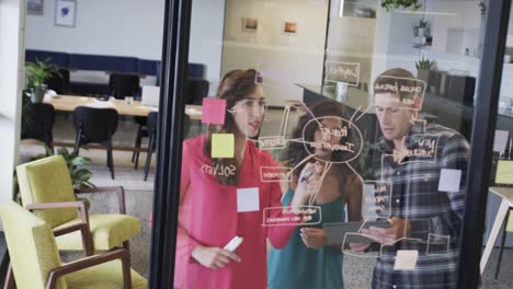 diverse creative colleagues in discussion making notes on glass wall in office, slow motion