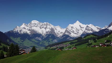 aerial video capturing majestic snow-capped mountains under a clear blue sky, with lush green hills