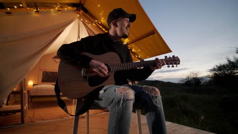 man plays the guitar and sings songs in a tent with light bulbs