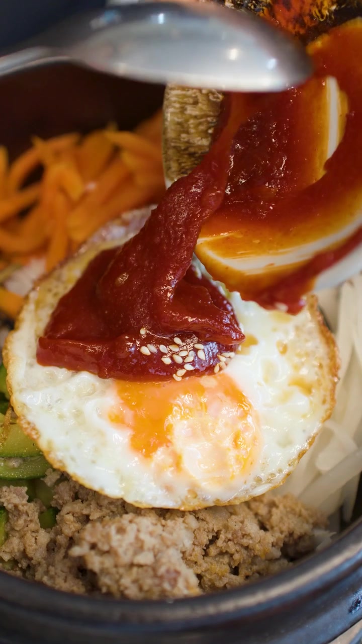 Sebuah bidikan jarak dekat menunjukkan pasta cabai merah disendokkan ke atas telur goreng dalam bibimbap.