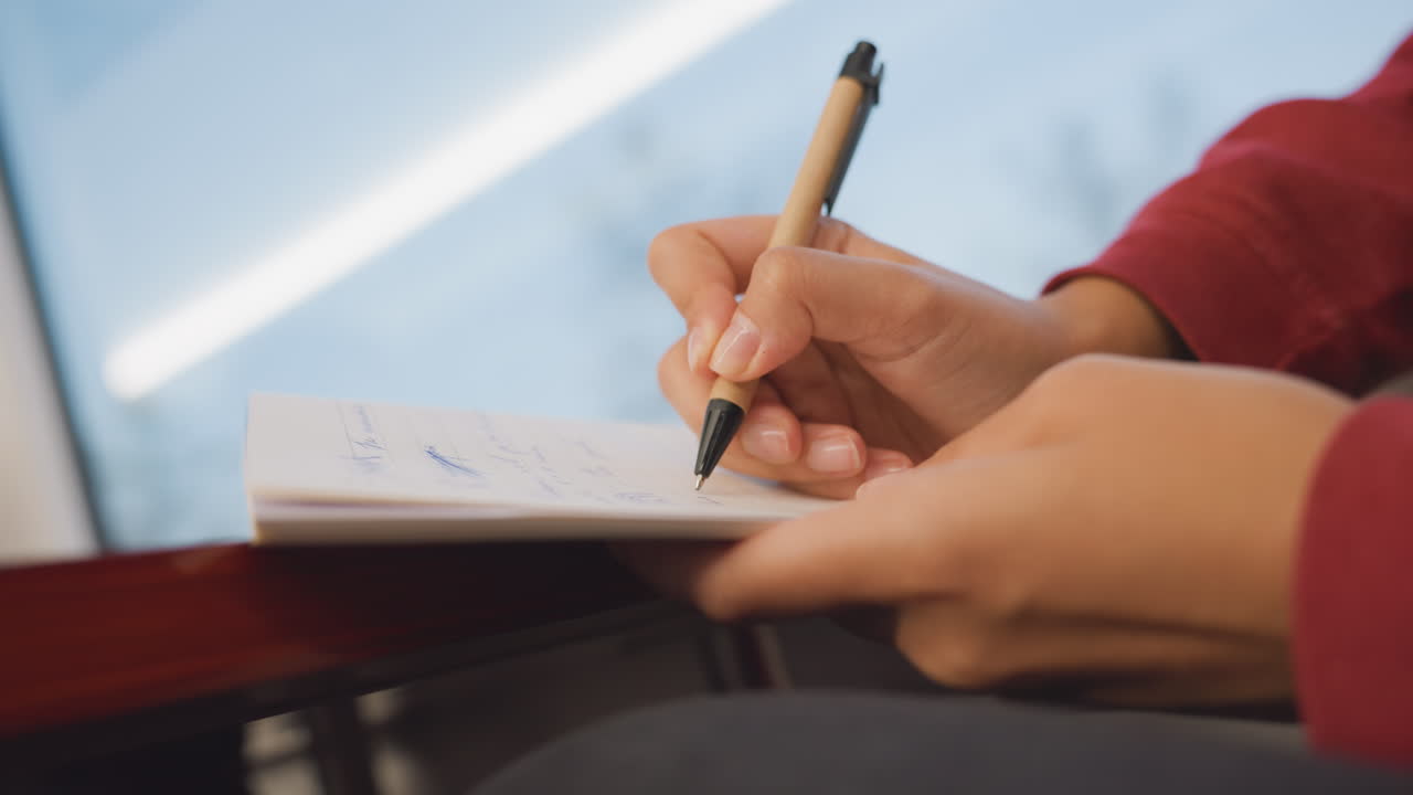 Student notes cafe. Focused student diligently taking notes in bustling urban coffeehouse environment. Individual carefully jotting down information during study session in lively city cafe setting
