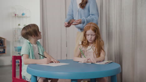 female teacher giving colored pencils to her pupils sitting at desk in montessori school 1