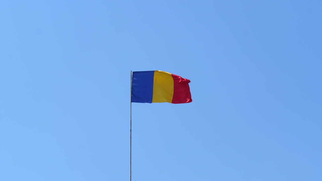 Flag Of Romania On Flagpole Fluttering In The Wind Against Clear Blue Sky