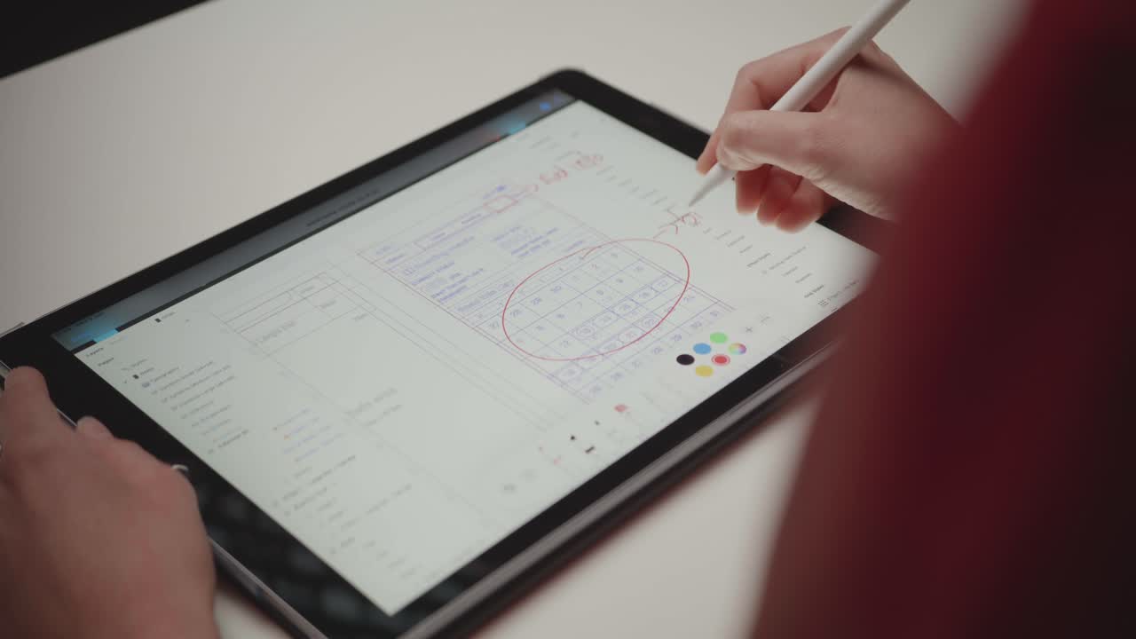 Over-the-shoulder shot of a person using a stylus to make notes and circle dates on a digital calendar app on a tablet. Concept of productivity, scheduling, and planning