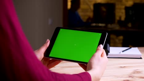 manos femeninas sosteniendo horizontalmente tableta con pantalla de croma verde en la oficina.