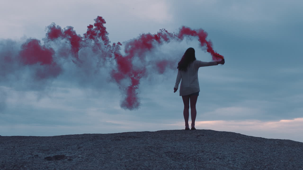 mujer joven jugando con granada de humo rosa bailando en la playa disfrutando de la libertad