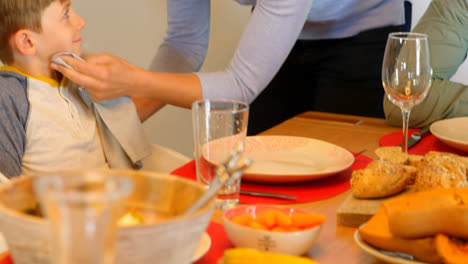 front view of young caucasian mother is wiping the sons mouth with a napkin cloth at dining table 4k