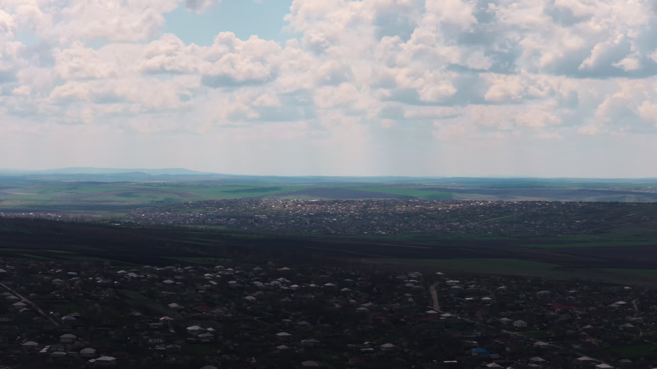 Moldova'da kırsal bir manzaranın havadan panoramik görünümü. Engebeli yeşil tepeler ve geniş tarım alanları arasına kurulmuş küçük köy evleri. Dramatik, bulutlu gökyüzü.