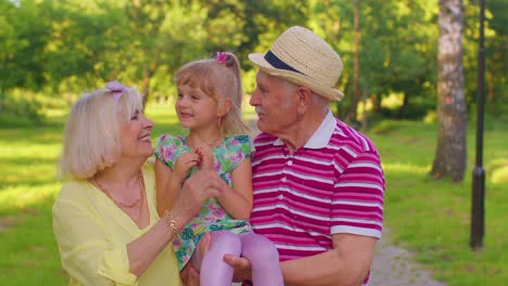 little cute granddaughter child embracing with her grandmother and grandfather family couple in park
