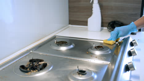 cleaning a kitchen stove surface. a person wearing a blue glove cleans a stainless steel stove with a sponge, making the kitchen tidy and hygienic