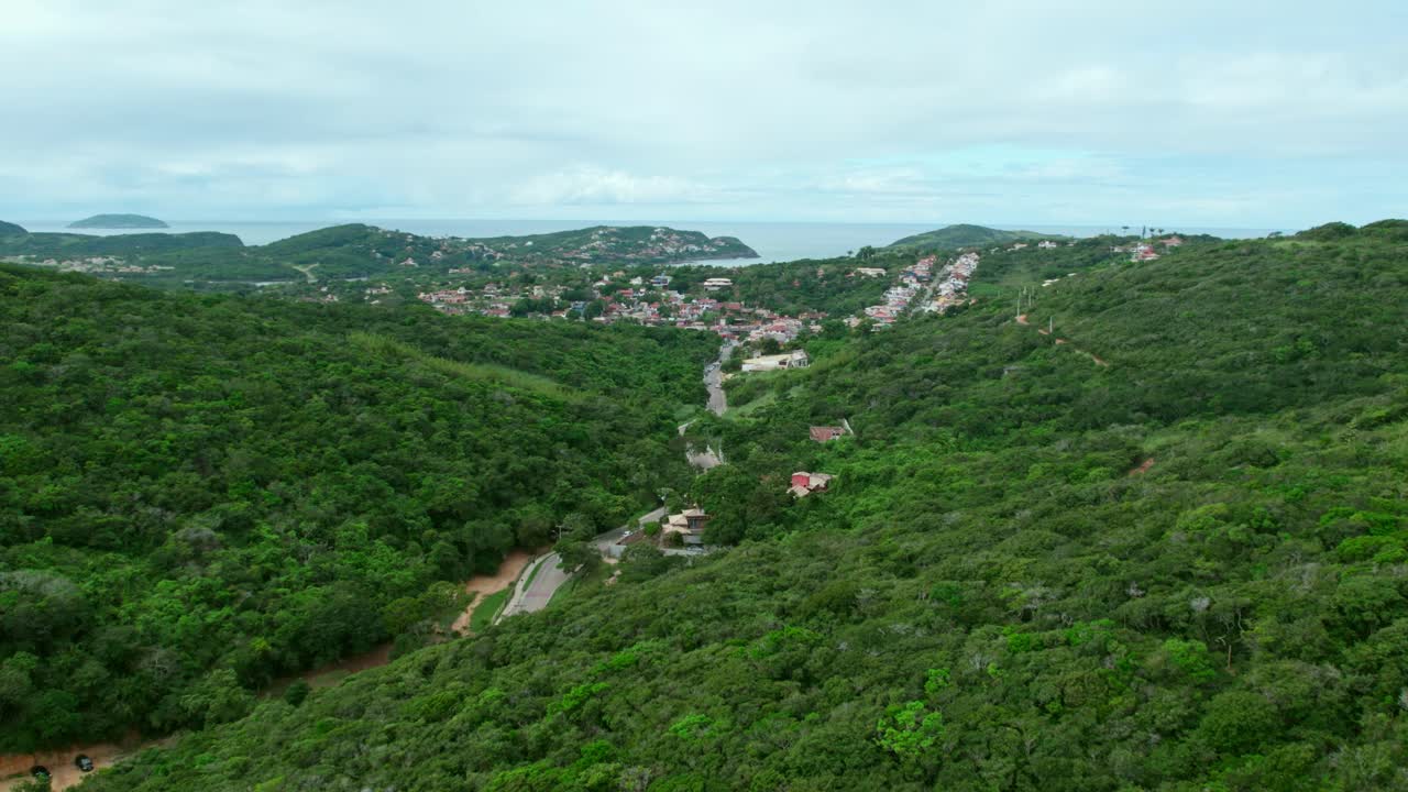Aerial view establishing dolly in B&uacute;zios hidden among lush mountains, Brazil