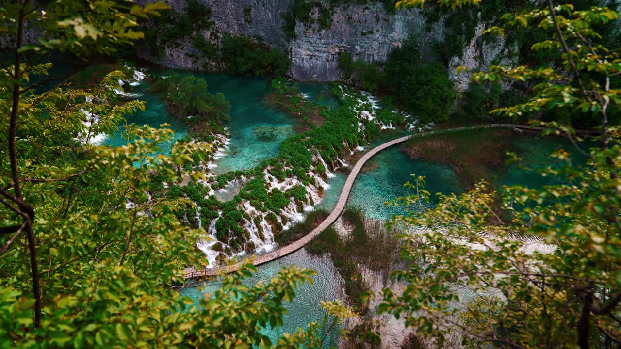 Scenic forest and waterfall landscape with wooden path across blue lake at Plitvice Lakes, Croatia