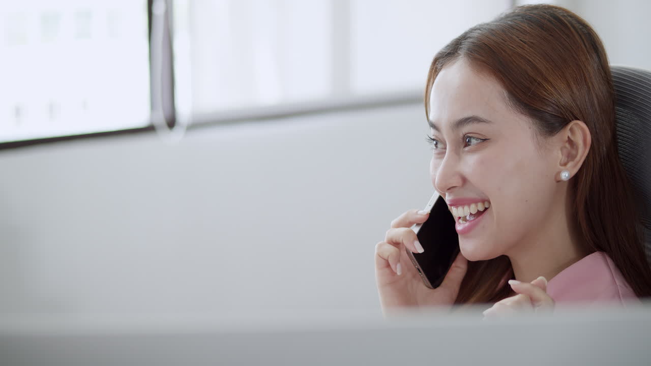 When making a mobile phone call, a young woman smiles and laughs while talking to someone.