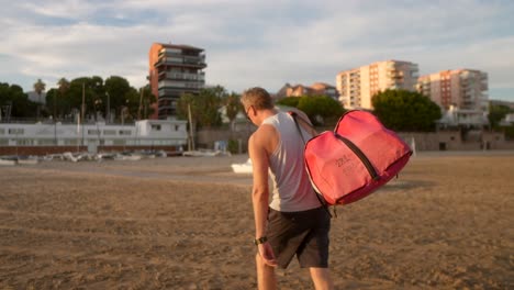 Hombre-Llevando-Las-Velas-De-Un-Catamarán-En-La-Playa-Al-Atardecer