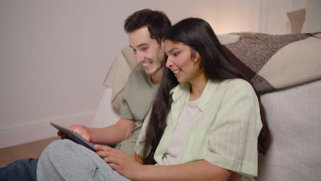 Side-View-Of-Couple-Watching-Interesting-Movie-On-Tablet-While-Sitting-On-The-Floor-At-Home